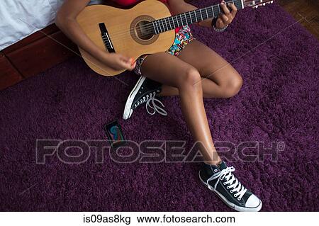 Stock Image - High angle chest down view of girl sitting on floor playing guitar. Fotosearch