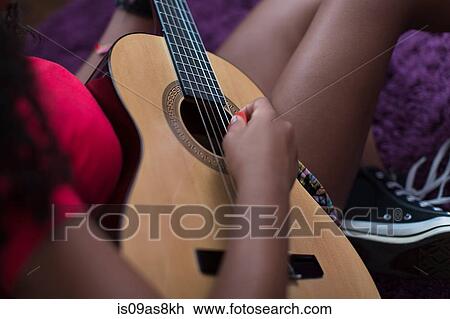 Stock Image - High angle cropped view of girl sitting on floor playing guitar. Fotosearch