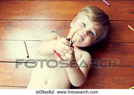 High angle view of boy lying on back on wooden floor holding crayons, looking at camera View Large Photo Image Stock Image - High angle view of boy lying on back on wooden floor holding crayons, looking at camera. Fotosearch