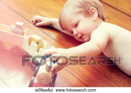 Stock Image - High angle view of boy lying on wooden floor playing with toy train. Fotosearch
