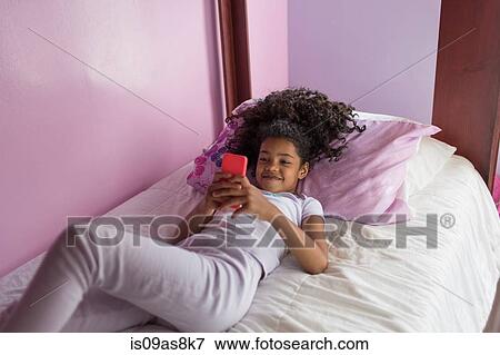 High angle view of girl wearing pyjamas lying on bed looking at smartphone View Large Photo Image Stock Photo - High angle view of girl wearing pyjamas lying on bed looking at smartphone. Fotosearch