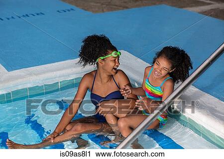 Stock Image - High angle view of girls sitting in swimming pool side by side laughing. Fotosearch