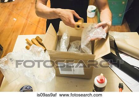 Stock Image - High angle view of young mans hands using bubble wrap to prepare parcel for delivery. Fotosearch