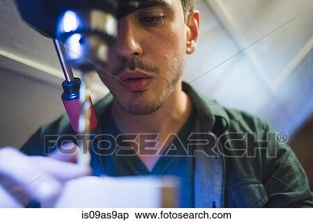 Stock Photography - Low angle view of young man using tool, face partially obscured. Fotosearch