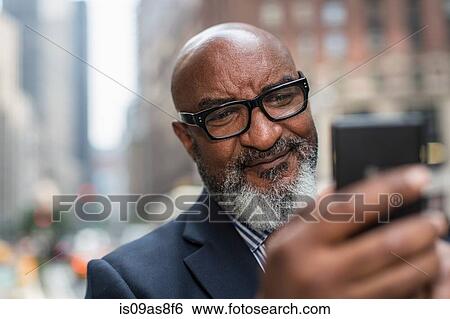 Stock Photograph - Mature businessman using smartphone on street. Fotosearch