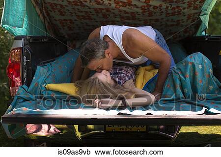 Stock Image - Mature man and girlfriend kissing in pick up boot whilst camping. Fotosearch