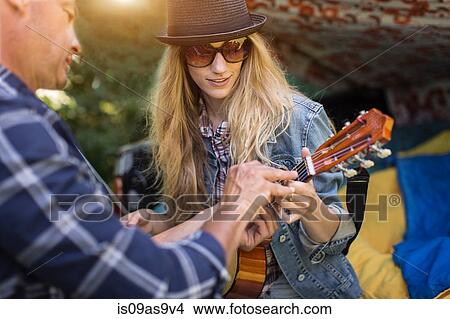 Picture - Mature man showing girlfriend how to play ukulele whilst camping in pick up boot. Fotosearch