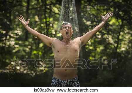 Stock Photo - Mature man with arms open under garden shower. Fotosearch