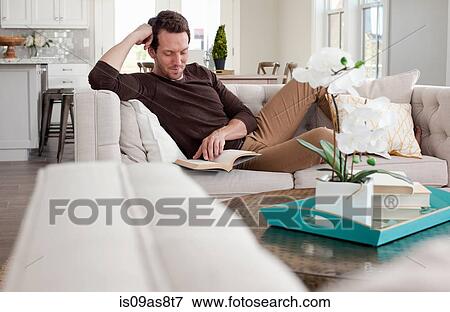 Mid adult man relaxing at home on sofa, reading book View Large Photo Image Stock Photo - Mid adult man relaxing at home on sofa, reading book. Fotosearch