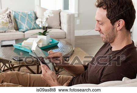 Mid adult man relaxing at home, using digital tablet View Large Photo Image Stock Photo - Mid adult man relaxing at home, using digital tablet. Fotosearch