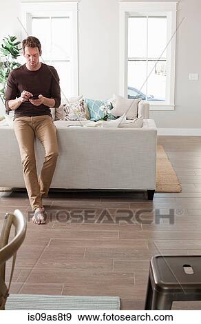 Mid adult man relaxing at home, using smartphone View Large Photo Image Stock Photo - Mid adult man relaxing at home, using smartphone. Fotosearch