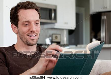 Mid adult man sitting at home, reading book View Large Photo Image Picture - Mid adult man sitting at home, reading book. Fotosearch