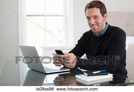 Mid adult man sitting at table, using laptop and smartphone View Large Photo Image Stock Image - Mid adult man sitting at table, using laptop and smartphone. Fotosearch