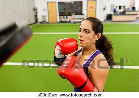 Stock Image - Mid adult woman wearing boxing gloves, working out in gym. Fotosearch