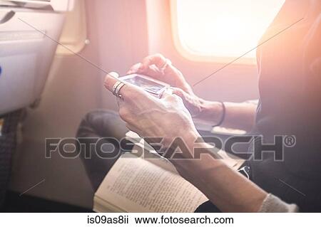 Stock Image - Person playing game on smartphone on board airplane. Fotosearch