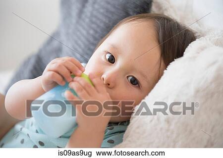 Stock Image - Portrait of baby boy on sofa drinking from baby cup. Fotosearch