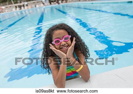 Stock Photograph - Portrait of girl in swimming pool wearing swimming goggles, looking at camera smiling. Fotosearch