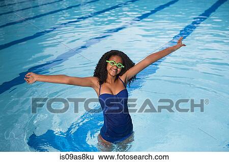 Portrait of girl standing in swimming pool wearing swimming goggles, arms raised, looking at camera smiling View Large Photo Image Stock Photograph - Portrait of girl standing in swimming pool wearing swimming goggles, arms raised, looking at camera smiling. Fotosearch