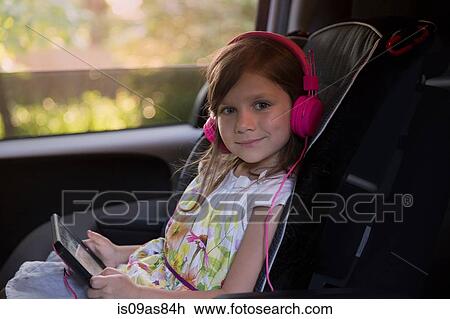 Portrait of girl wearing pink headphones and using digital tablet in car View Large Photo Image Stock Image - Portrait of girl wearing pink headphones and using digital tablet in car. Fotosearch