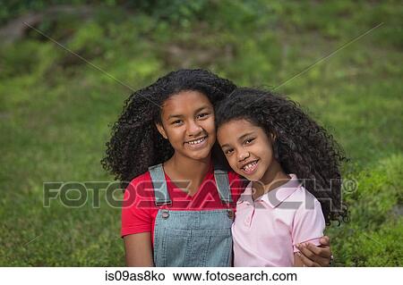 Portrait of girl with arm around her sister, looking at camera smiling View Large Photo Image Picture - Portrait of girl with arm around her sister, looking at camera smiling. Fotosearch