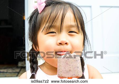 Stock Image - Portrait of young girl, eating ice lolly. Fotosearch