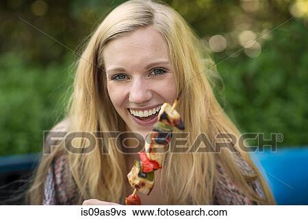 Stock Photograph - Portrait of young woman holding barbecued kebab stick. Fotosearch