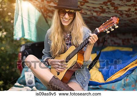 Stock Photography - Portrait of young woman playing ukulele whilst camping in pick up boot. Fotosearch