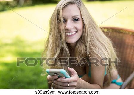 Portrait of young woman wearing bikini using smartphone in garden View Large Photo Image Picture - Portrait of young woman wearing bikini using smartphone in garden. Fotosearch