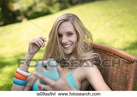 Portrait of young woman wearing bikini top using smartphone in garden View Large Photo Image Stock Image - Portrait of young woman wearing bikini top using smartphone in garden. Fotosearch
