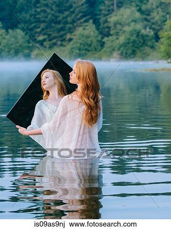Rear view of young woman standing in lake holding mirror looking away View Large Photo Image Stock Image - Rear view of young woman standing in lake holding mirror looking away. Fotosearch