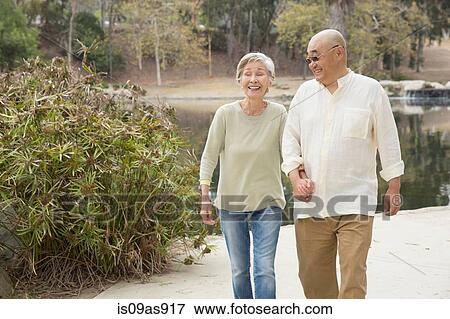 Senior couple walking along pathway, holding hands, laughing View Large Photo Image Stock Photo - Senior couple walking along pathway, holding hands, laughing. Fotosearch