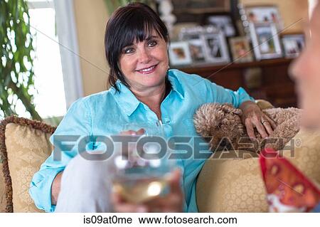 Stock Image - Senior woman at home, sitting on sofa, talking to friend. Fotosearch