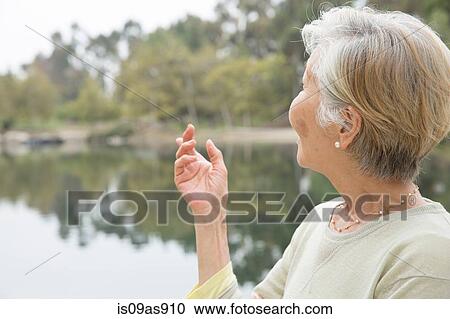 Stock Image - Senior woman beside lake, rear view. Fotosearch