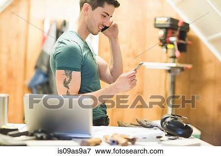 Stock Photo - Side view of young man talking on telephone looking at credit card smiling. Fotosearch
