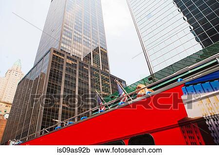 Stock Image - Sight seeing bus with office buildings, low angle view, New York, USA. Fotosearch