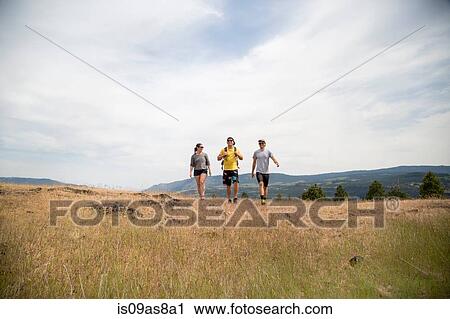 Stock Image - Small group of friends hiking through field. Fotosearch