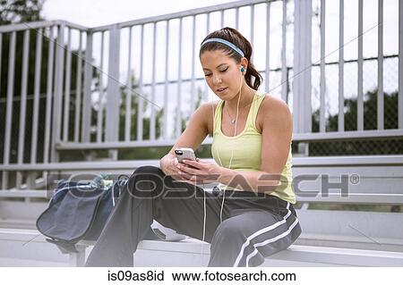 Stock Image - Soccer player using smartphone on bench. Fotosearch