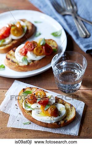 Stock Image - Still life of bruschetta with roasted cherry tomatoes, buffalo mozzarella, fresh oregano and pepper. Fotosearch