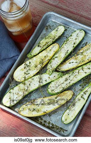 Stock Image - Still life of roasted baby courgettes with thyme, olive oil and cup of iced tea. Fotosearch