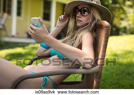 Sultry young woman wearing bikini and sunglasses reading smartphone texts in garden View Large Photo Image Stock Image - Sultry young woman wearing bikini and sunglasses reading smartphone texts in garden. Fotosearch