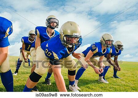 Team of teenage and adult American football players hunkering down on practice field View Large Photo Image Stock Photo - Team of teenage and adult American football players hunkering down on practice field. Fotosearch