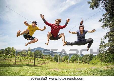 Stock Image - Three adults jumping in rural setting, mid air, laughing. Fotosearch