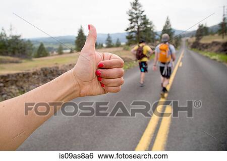 Two men hiking along road, while woman thumbs a lift, focus on hand View Large Photo Image Stock Photograph - Two men hiking along road, while woman thumbs a lift, focus on hand. Fotosearch