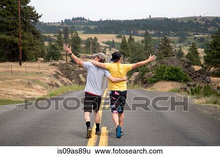 Two men walking along road together, arms raised, appreciating view, rear view View Large Photo Image Stock Photograph - Two men walking along road together, arms raised, appreciating view, rear view. Fotosearch
