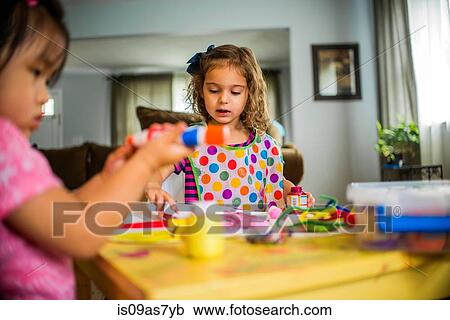 Two young girls sitting at table, making art, using paint View Large Photo Image Stock Image - Two young girls sitting at table, making art, using paint. Fotosearch
