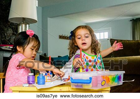 Two young girls sitting at table, making art, using paint View Large Photo Image Stock Image - Two young girls sitting at table, making art, using paint. Fotosearch
