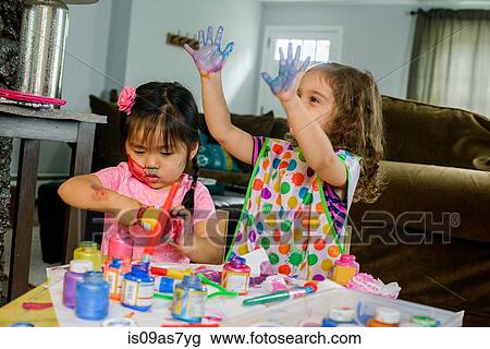 Two young girls sitting at table, making art, using paint View Large Photo Image Stock Image - Two young girls sitting at table, making art, using paint. Fotosearch
