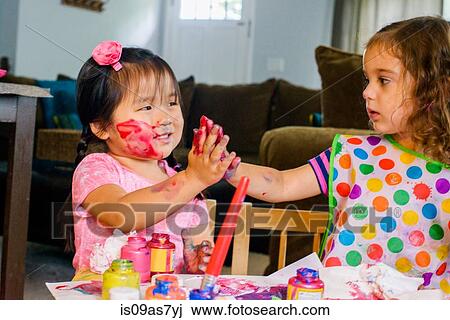 Two young girls sitting at table, making art, using paint View Large Photo Image Stock Image - Two young girls sitting at table, making art, using paint. Fotosearch