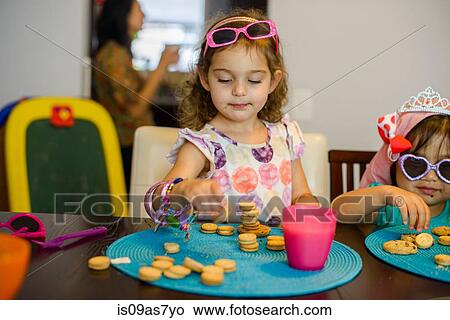 Two young girls sitting at table with drink and cookies View Large Photo Image Picture - Two young girls sitting at table with drink and cookies. Fotosearch
