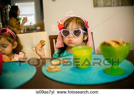 Two young girls sitting at table with drink and cookies View Large Photo Image Stock Image - Two young girls sitting at table with drink and cookies. Fotosearch